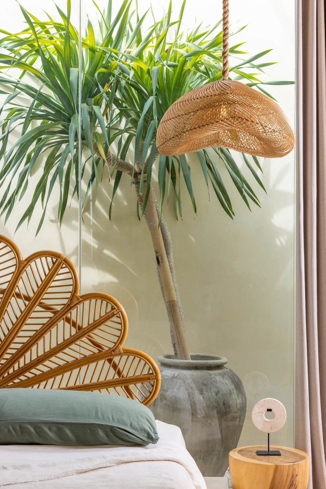 Bayu Rattan Lampe hängt neben einem Bett vor einem Fenster